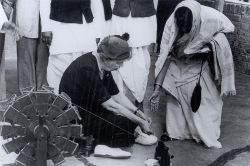 Eleanor Roosevelt kneeling on the ground next to a spinning wheel