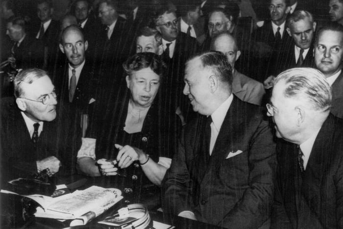 Eleanor Roosevelt in a crowded room leaning over to talk to a man